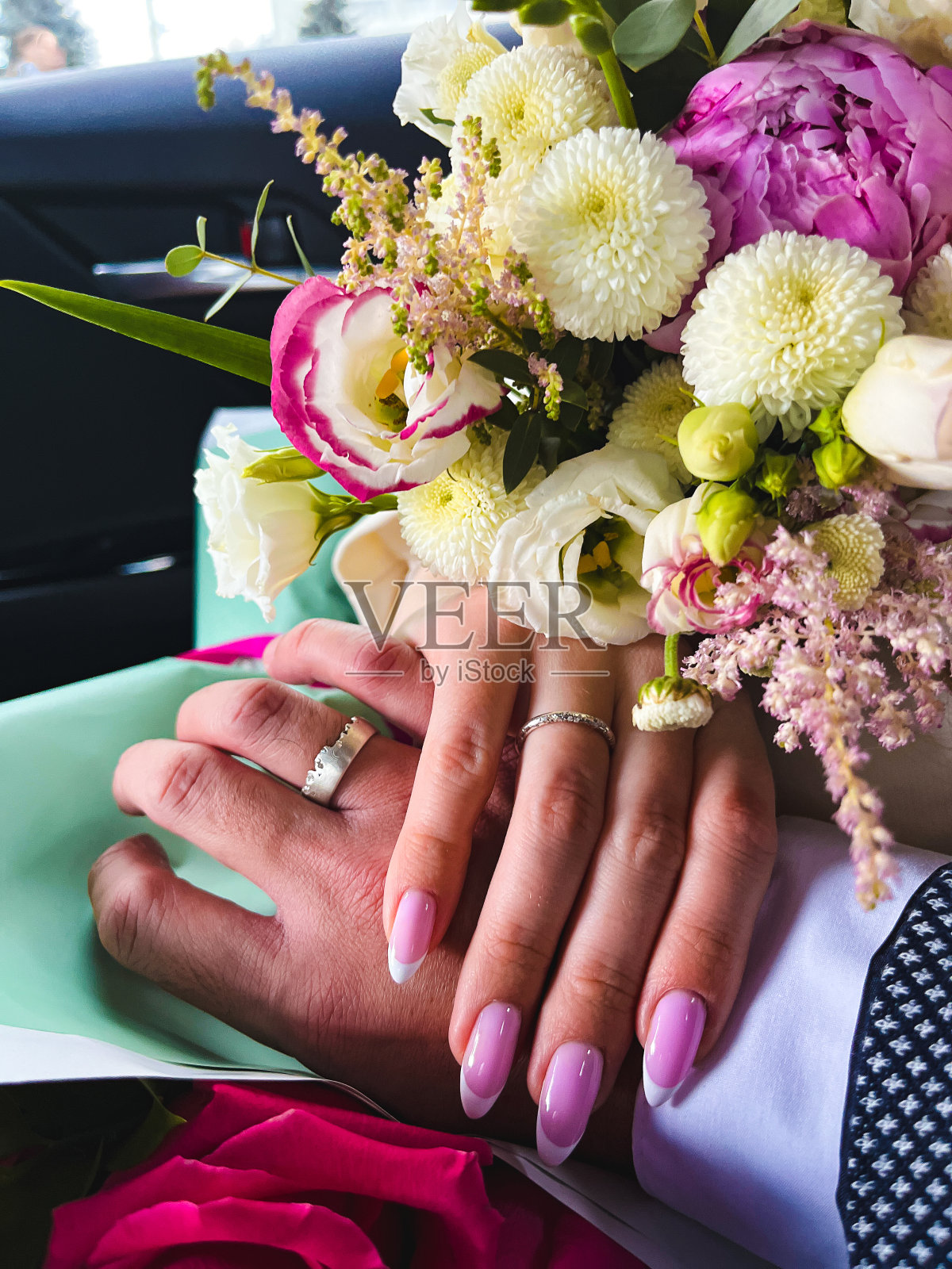 新婚夫妇手牵着手，在车里的鲜花背景上展示他们的结婚戒指照片摄影图片