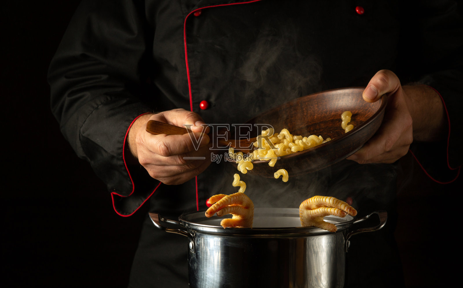 厨师用手把意面加到一锅沸腾的鸡腿上。在餐厅或酒店的厨房里准备美味汤的概念照片摄影图片