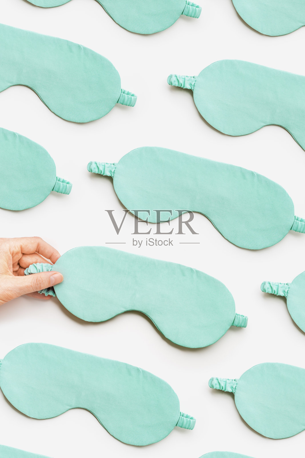 最小的图案从丝绸睡眠面具在白光背景。女士手拿绿松石色眼罩，舒适休息，优质睡眠的理念。创意美学的俯视图构图照片摄影图片