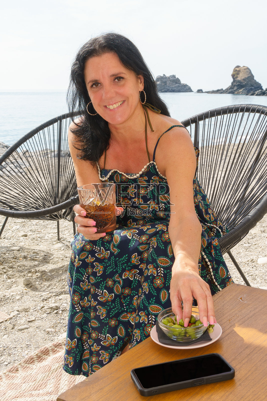 一个女人坐在海边的酒吧里，喝着软饮料，吃着橄榄。照片摄影图片