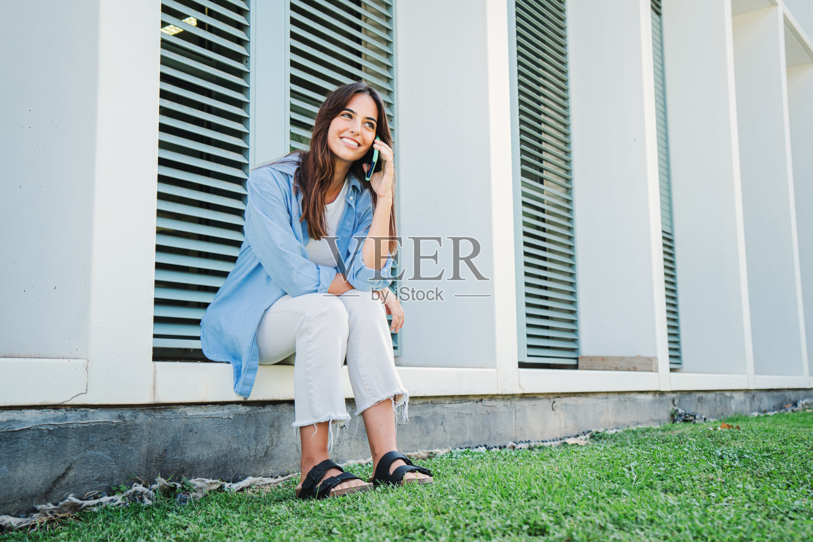年轻的高加索女人微笑着用手机说话。在外面休息的女士正在用智能手机友好地打电话。快乐的女学生用手机订外卖。照片摄影图片