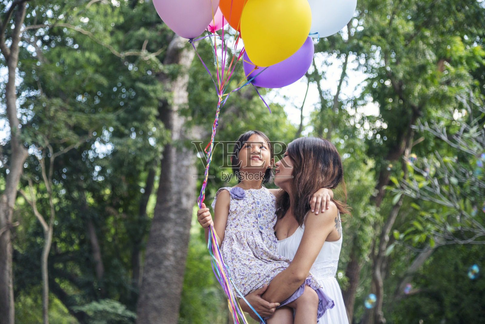 幸福的妈妈女儿一起在绿色花园公园玩气球户外的生活方式。幸福的家庭两个人享受有乐趣愉快的微笑。妈妈小时候手捧着五颜六色的气球在外面照片摄影图片