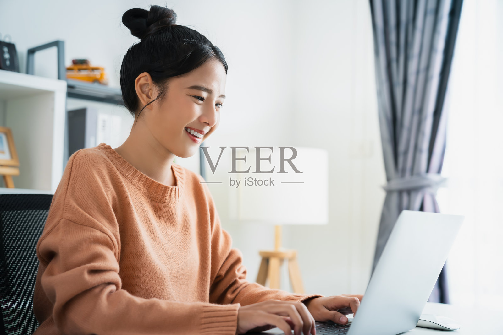 年轻漂亮的女性坐在办公桌前使用笔记本电脑。照片摄影图片