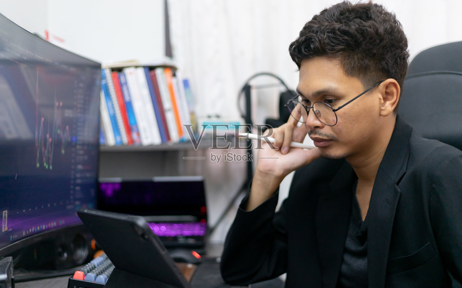 成功的亚洲男性交易员分析股票市场和交易所的价格图表在网站上。一名家庭金融投资交易员，使用平板电脑和个人电脑进行股票和商品交易。照片摄影图片