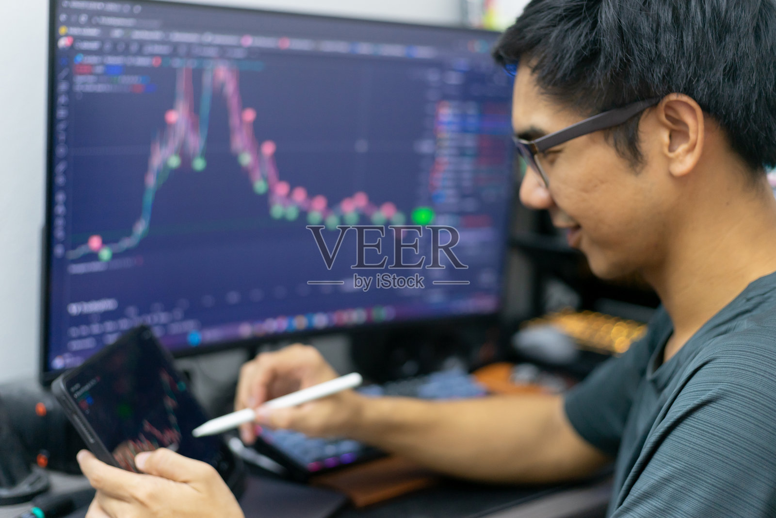 成功的亚洲男性交易员分析股票市场和交易所的价格图表在网站上。一名家庭金融投资交易员，使用平板电脑和个人电脑进行股票和商品交易。照片摄影图片