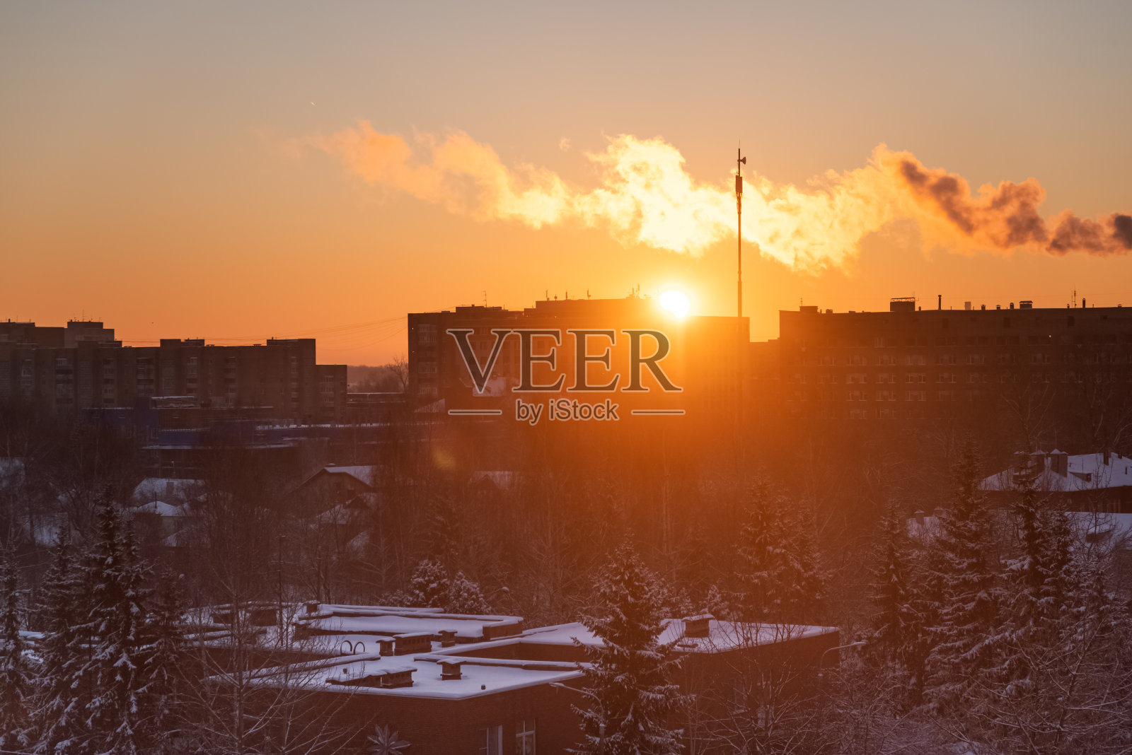 在夕阳的映衬下，从工厂管道或烟囱里冒出的烟雾在住宅区的屋顶上蔓延。环境污染、城市生态、城镇工业区照片摄影图片