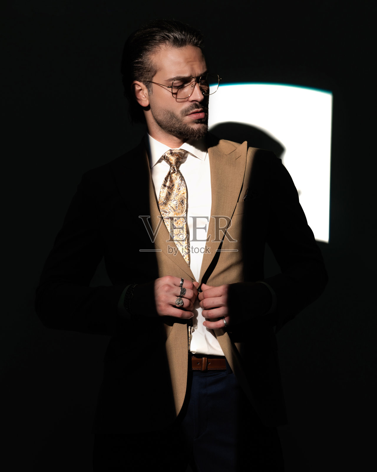 酷酷的年轻商人，眼镜朝下，西装紧扣照片摄影图片