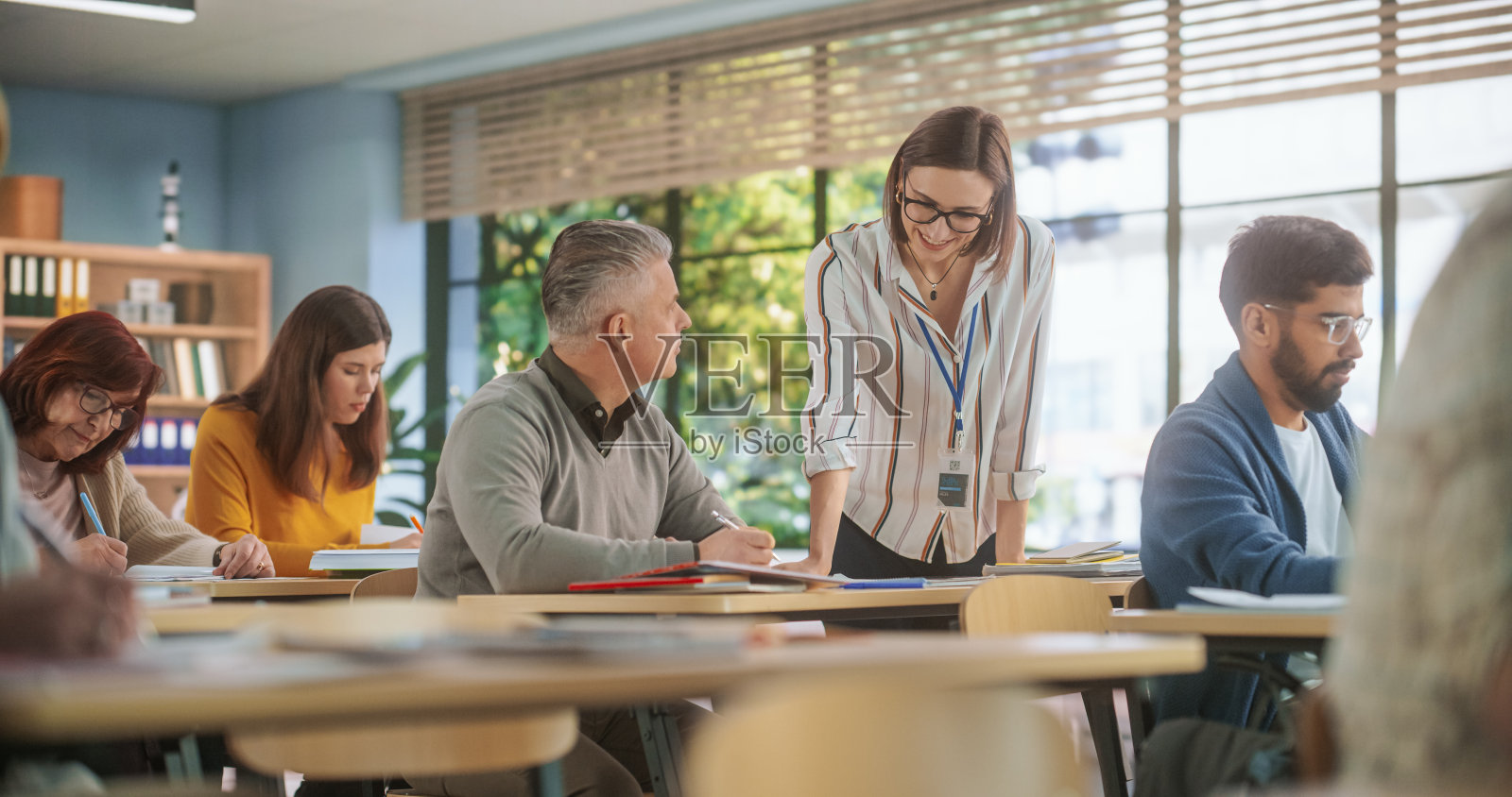 乐于助人的年轻老师与一个成年男子谈话，帮助找到解决考试课程作业的方法。不同年龄的多民族男女在课堂上获得新的学术技能照片摄影图片