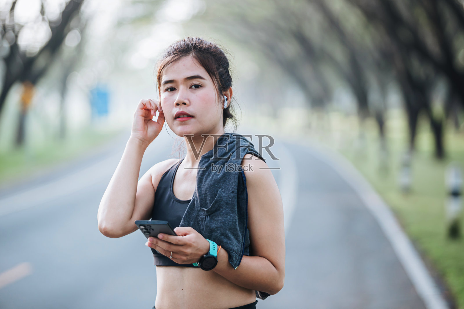 年轻的健身女性在公园里用智能手机听音乐。照片摄影图片