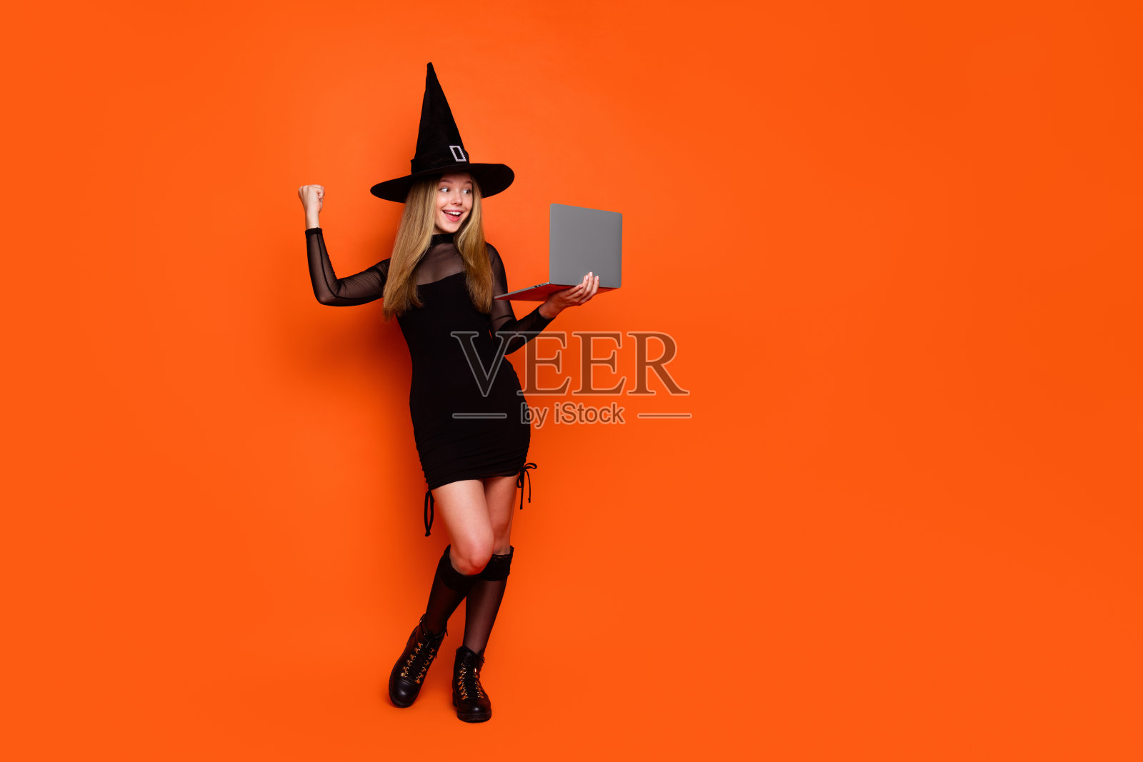 漂亮的金发少女的全尺寸照片赢得了笔记本电脑穿着黑色万圣节服装孤立的橙色背景照片摄影图片