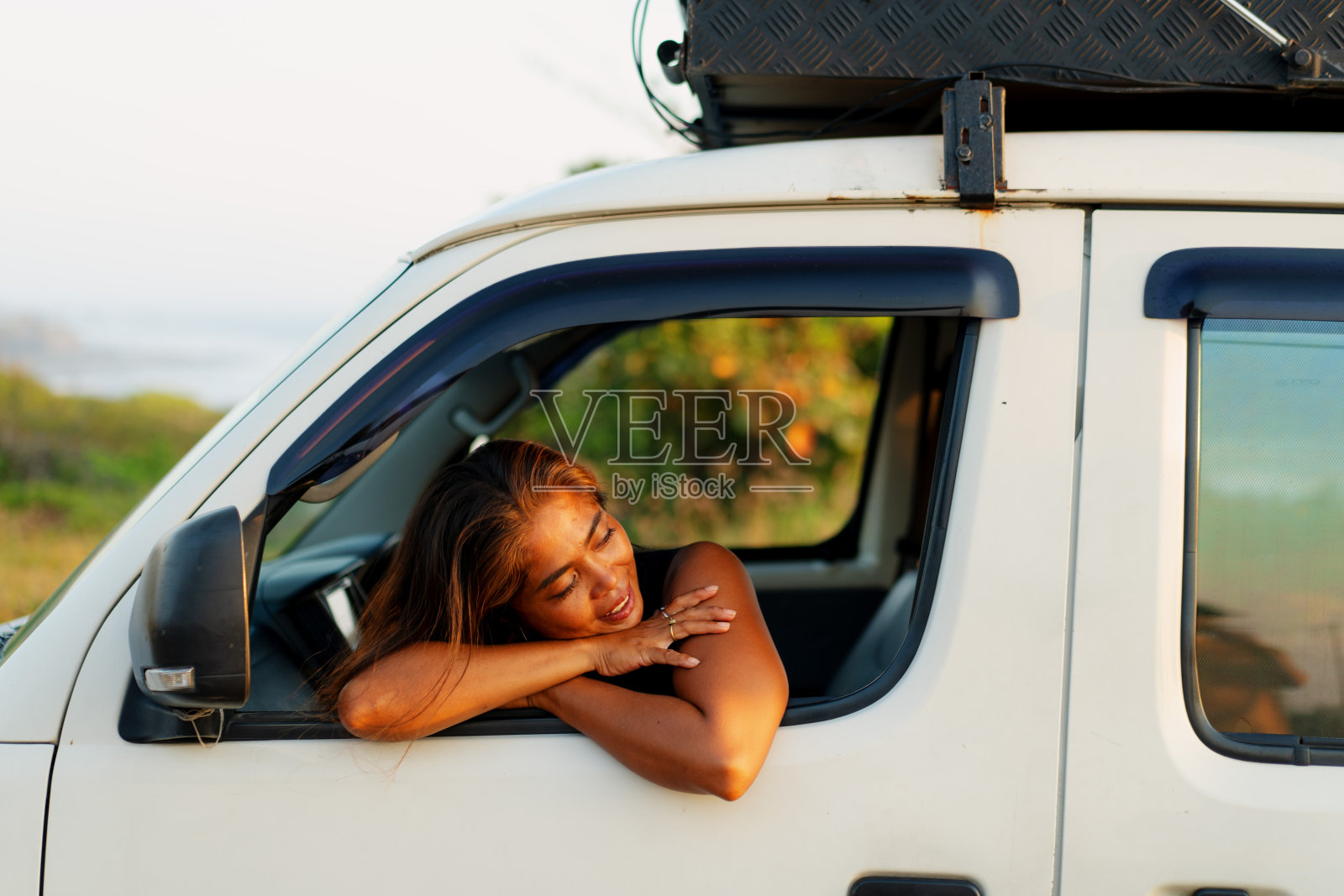 一名东南亚女子坐在车里，把头伸出窗外欣赏日落照片摄影图片