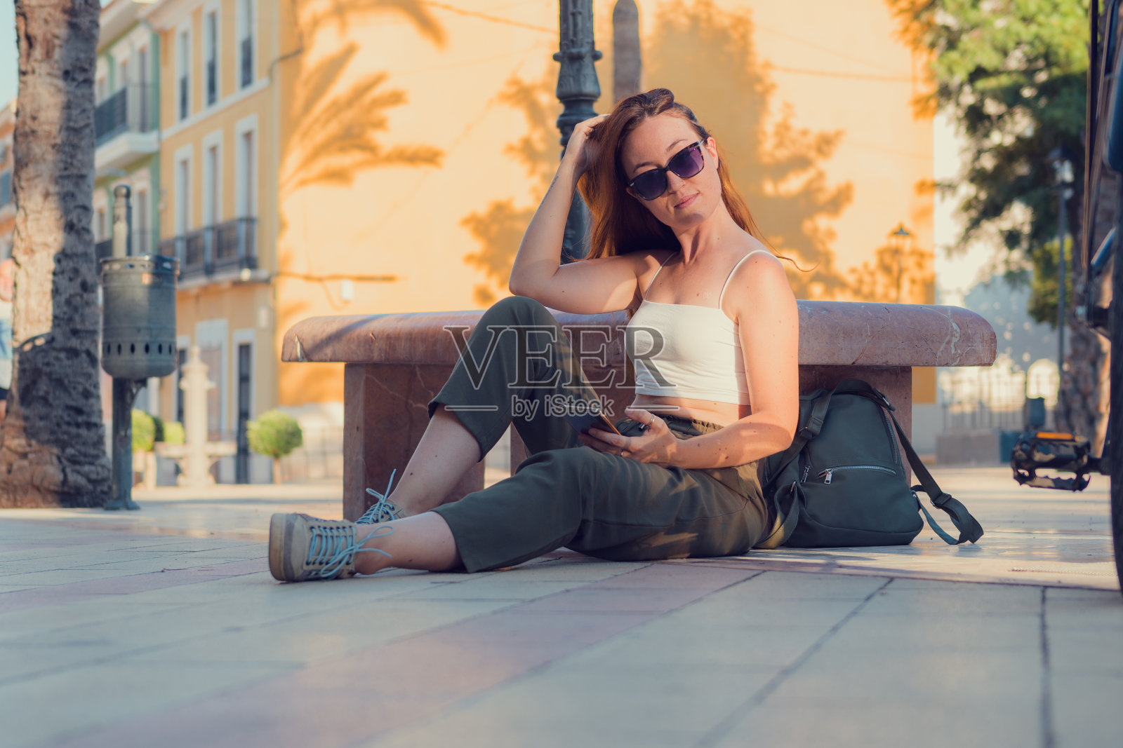 一名年轻女子带着手机和太阳镜在小镇上摆姿势照片摄影图片