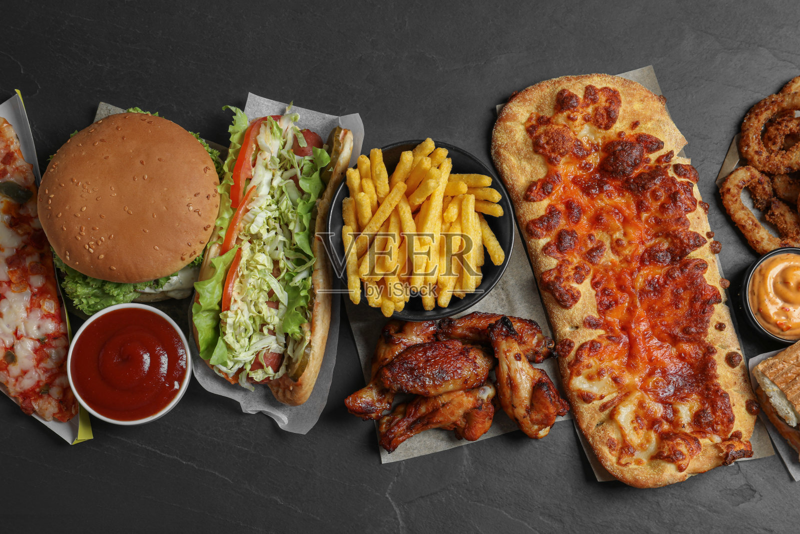 汉堡、披萨等快餐在黑色的桌子上，平躺着照片摄影图片