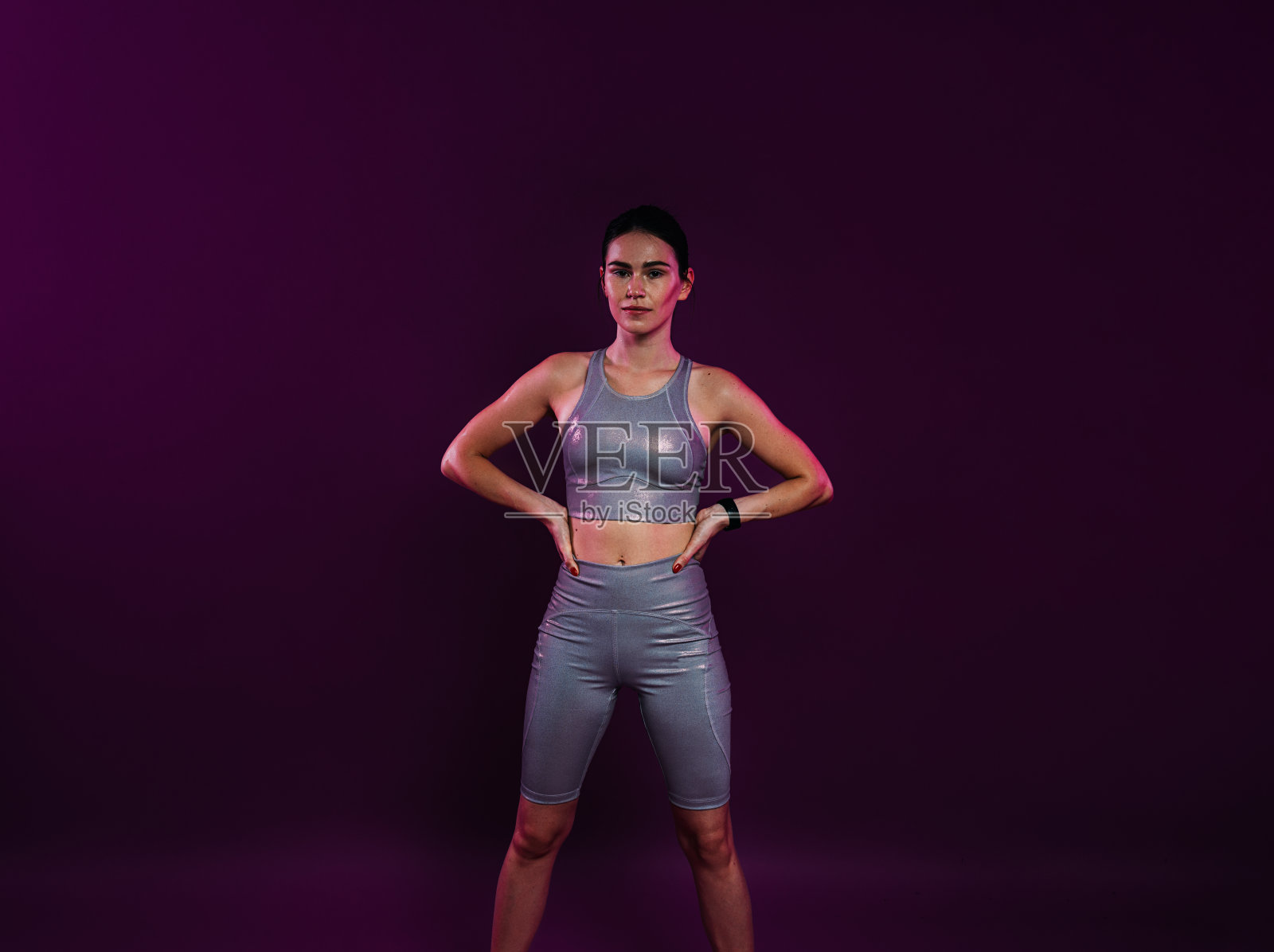 年轻自信的女运动员，身穿银色健身服，双手叉腰照片摄影图片