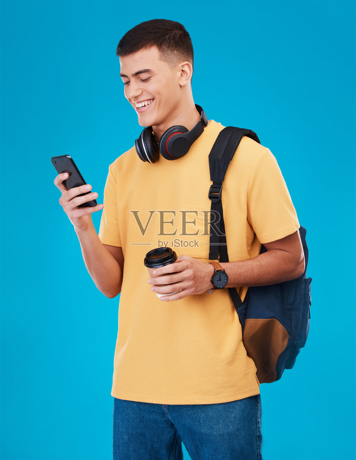 微笑，手机，一个学生或男人，在蓝色背景上喝咖啡，用于社交媒体。快乐，联系和一个年轻的z世代的人从一个应用程序在手机上阅读教育或学习网站照片摄影图片