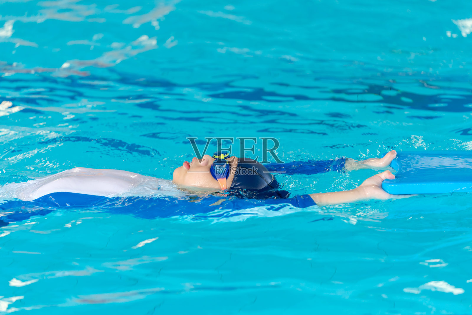 一个小男孩的活力去游泳池做仰泳练习。游泳池清澈的蓝色海水为他的水上活动提供了完美的背景。穿上泳装，戴上护目镜，自信地踏上健康之旅。照片摄影图片