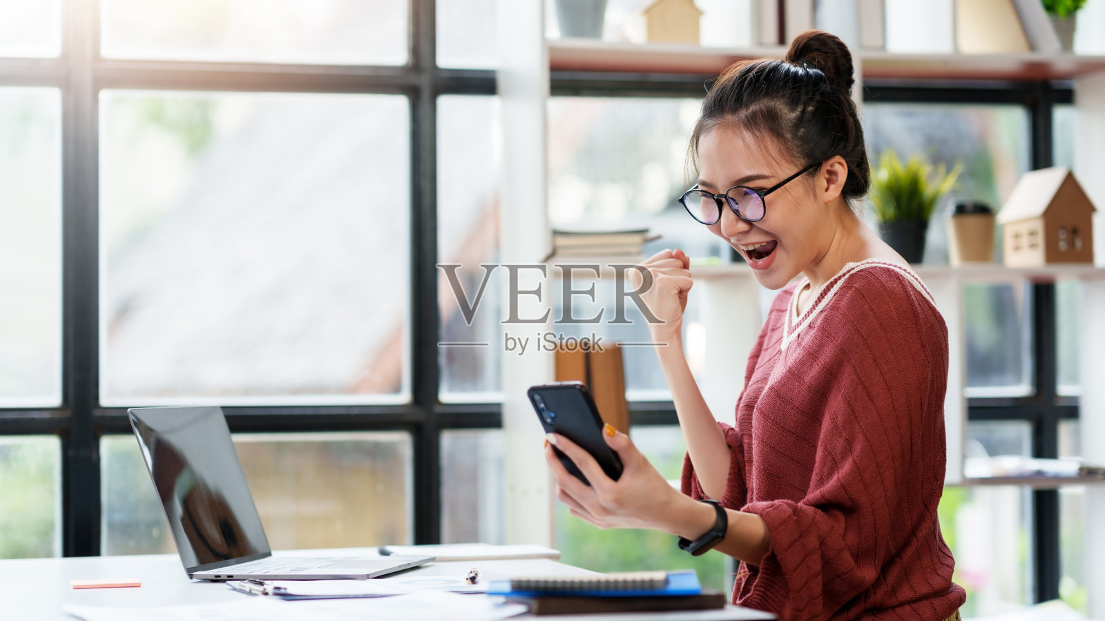 漂亮的亚洲女商人在办公室里举着手机，为自己的成功感到兴奋。照片摄影图片