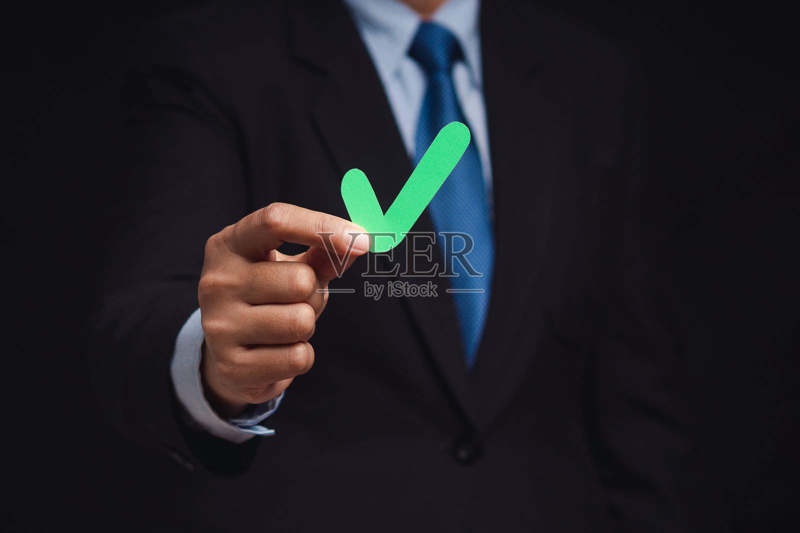 一个商人站在黑色的背景上，手里拿着一个绿色的勾号符号照片摄影图片