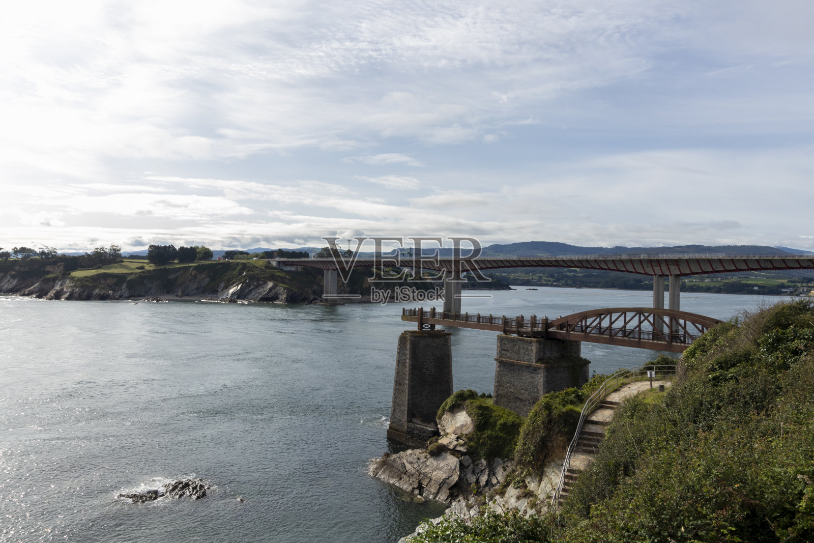 多云的天空下，平静的河流上的弯曲桥的宁静景色照片摄影图片