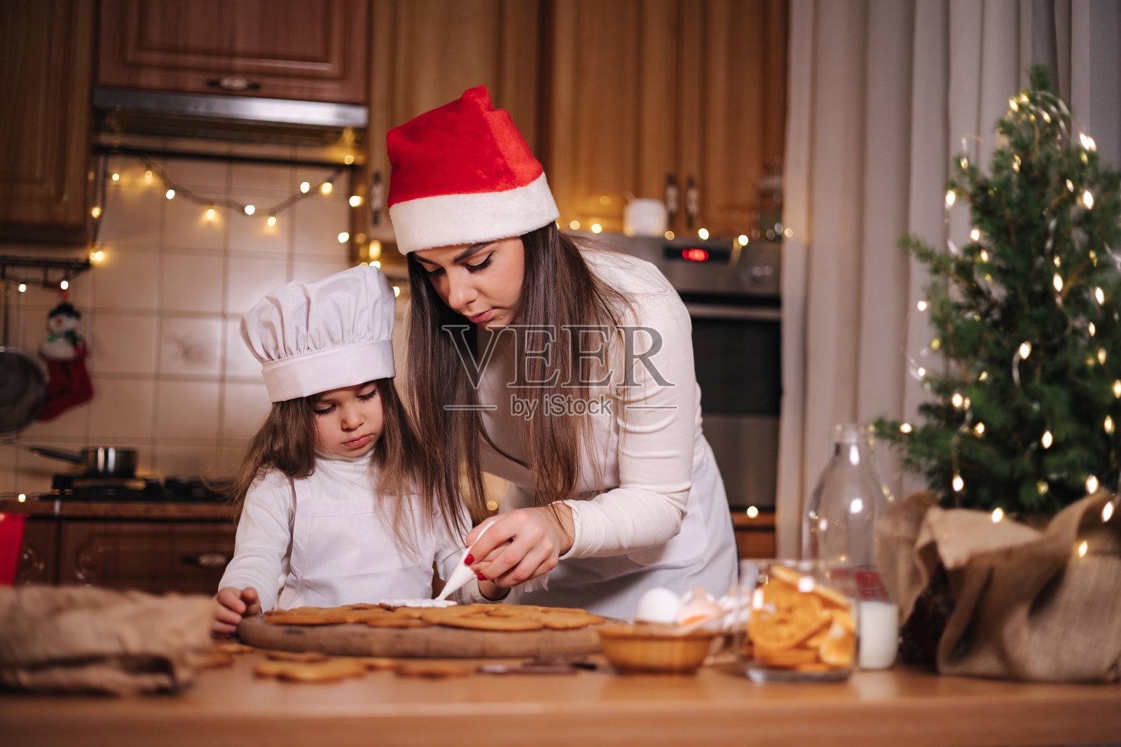 快乐的小女孩和她美丽的妈妈在家里做姜饼。厨房的圣诞装饰。有仙女灯的冷杉树照片摄影图片