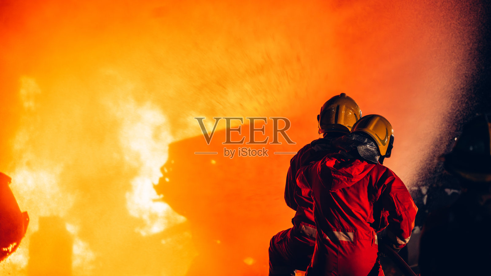 无畏的消防员用水和灭火器灭火。行动中的消防员，以团队精神和勇气灭火。激烈的消防训练演习。照片摄影图片