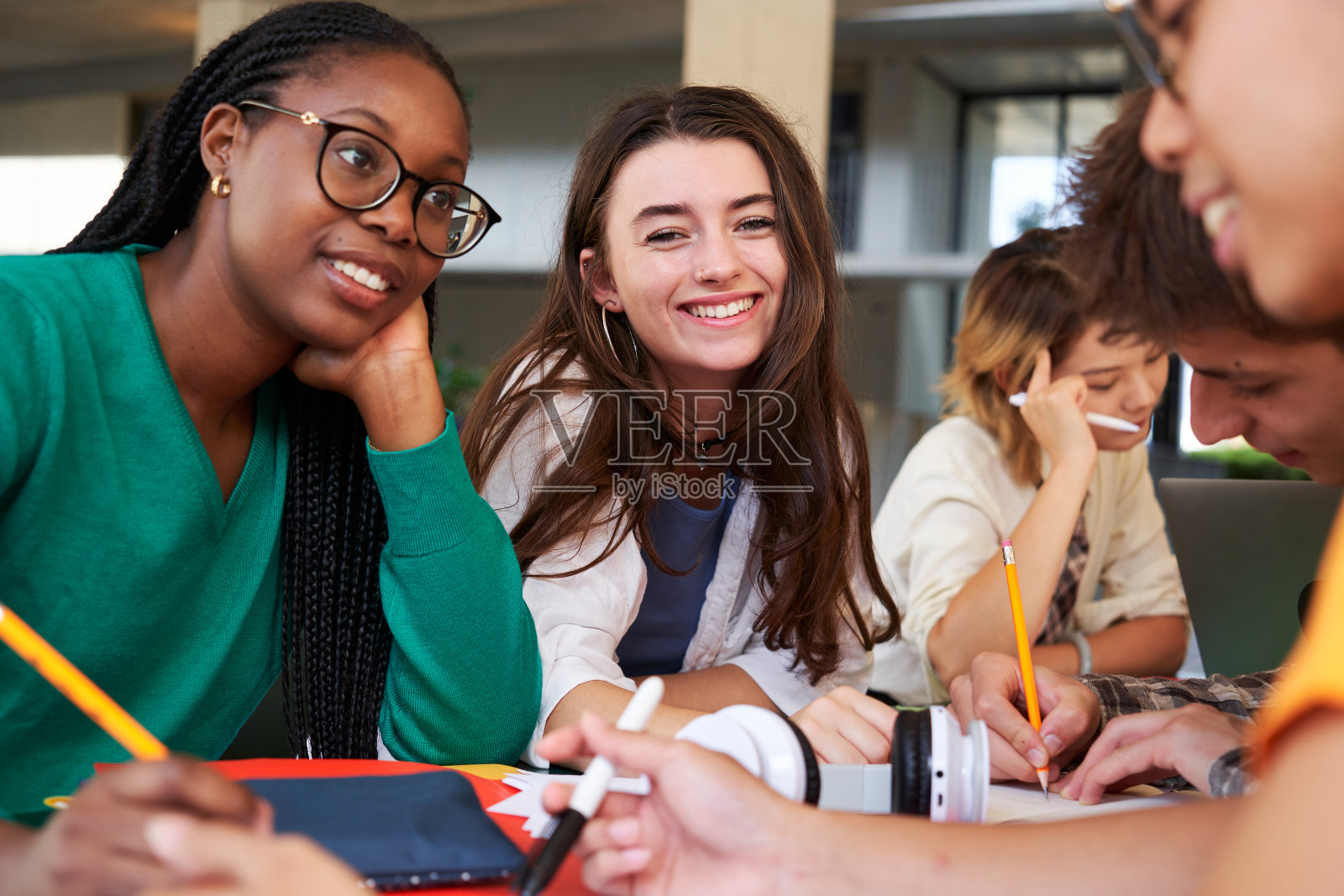 年轻的学生女孩看着镜头，而坐在她的朋友们团聚在一起学习。照片摄影图片