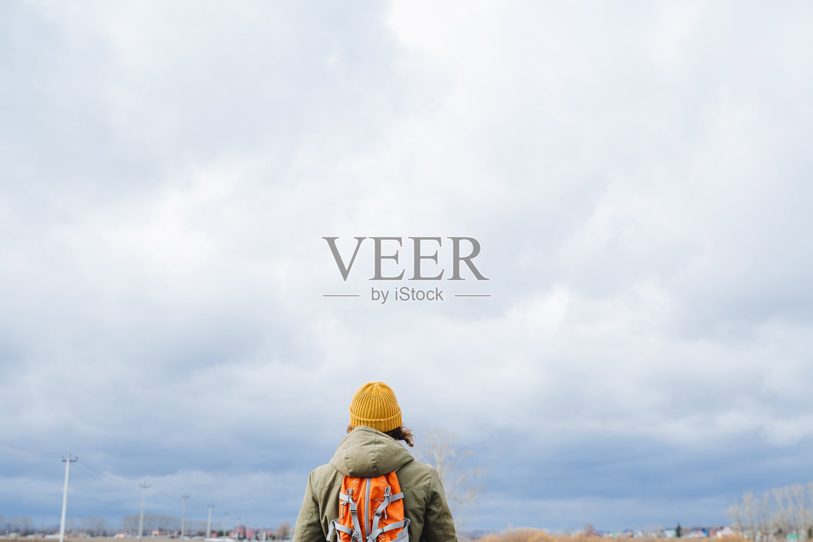 从后面看，一个人肩上背着背包，戴着一顶黄色的帽子，一个游客背对着天空站着，多云的天气，徒步的云，孤独，寂静。照片摄影图片