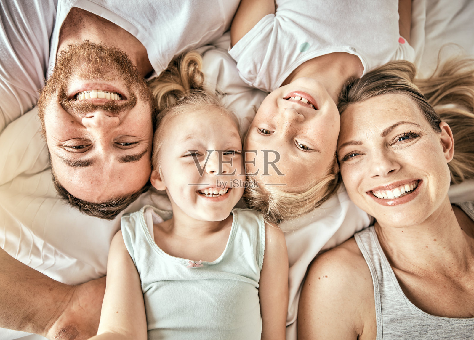 在现代家庭中，快乐，微笑和家庭肖像在床上建立联系和放松。幸福，爱和俯视图的女孩躺在卧室里的父母来自澳大利亚。照片摄影图片