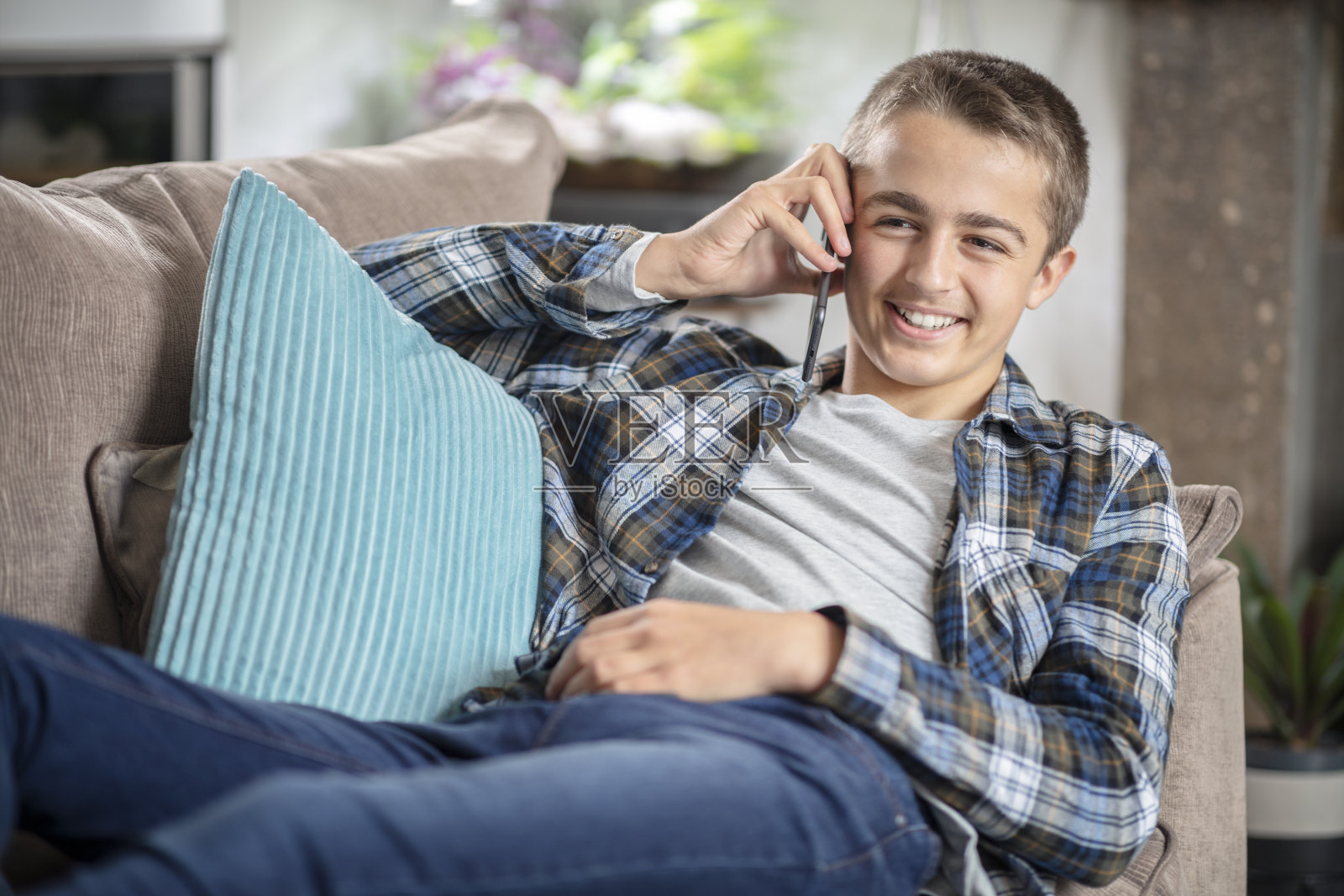 男孩坐在沙发上讲手机，开心和微笑的背景照片摄影图片