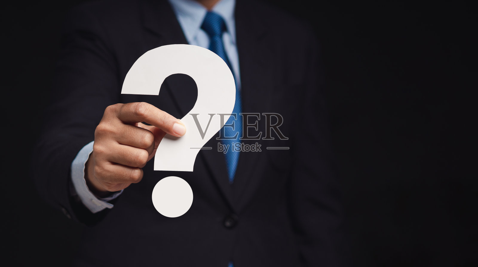 商人站在黑色的背景上，手里拿着一张白色的问号纸照片摄影图片