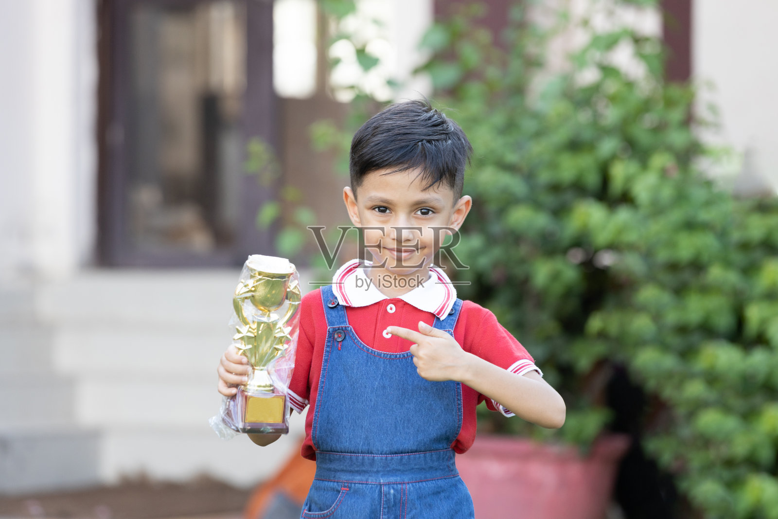 快乐的印度学生在校园里穿着校服，手拿胜利奖杯。教育的概念。照片摄影图片