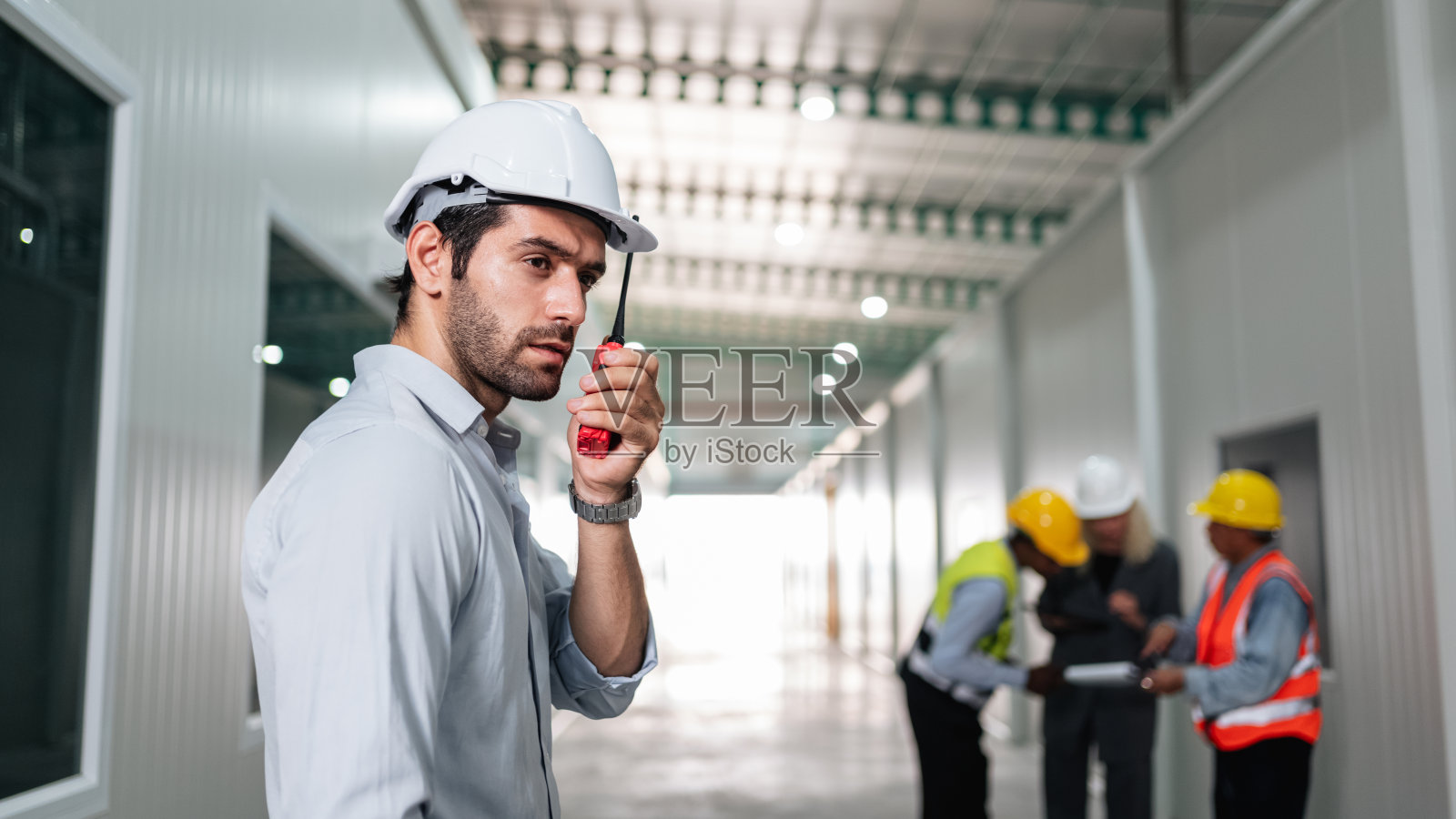 图为工程师和工人在空荡荡的仓库里用对讲机设计产品货架的布置。照片摄影图片