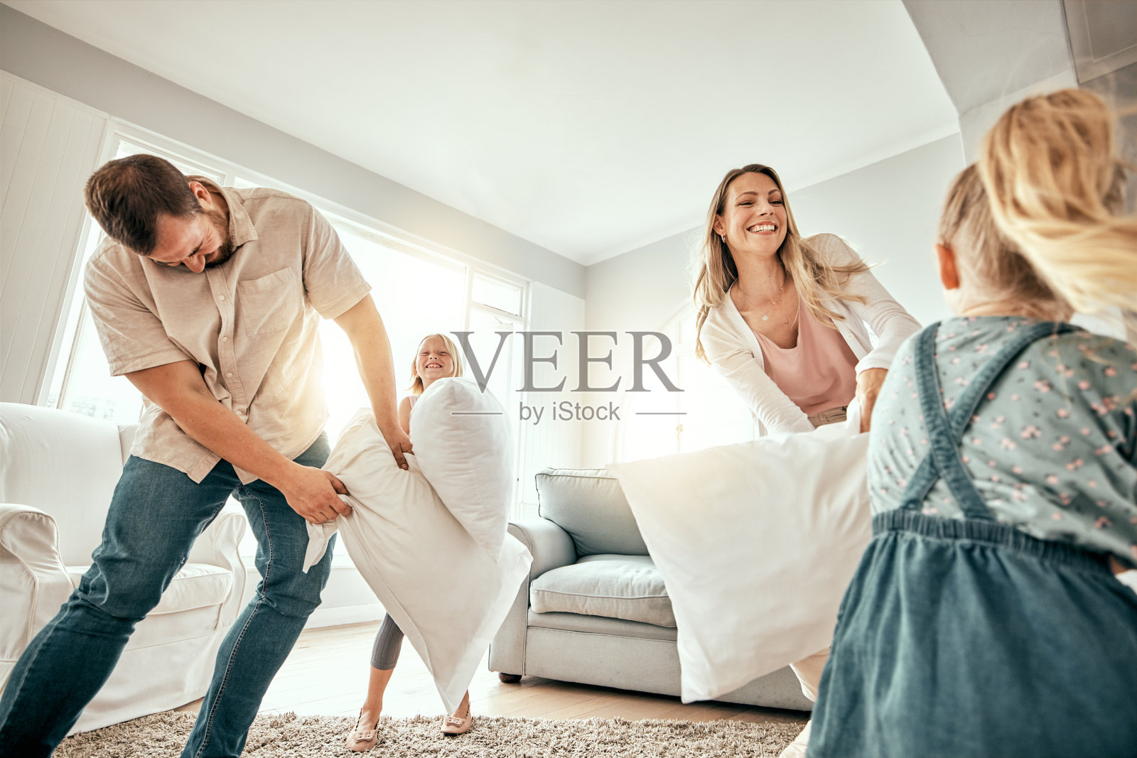 快乐的家庭，枕头大战和在客厅玩耍的乐趣结合，假期或周末在家里一起。妈妈、爸爸和孩子们笑着用垫子玩游戏，暑假还是玩的自由时间照片摄影图片