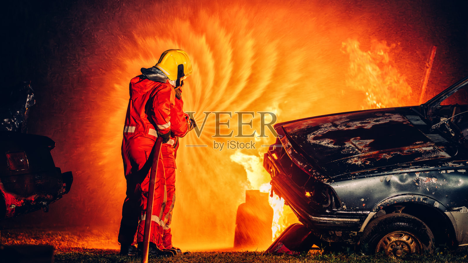 无畏的消防员用水和灭火器灭火。行动中的消防员，以团队精神和勇气灭火。激烈的消防训练演习。照片摄影图片