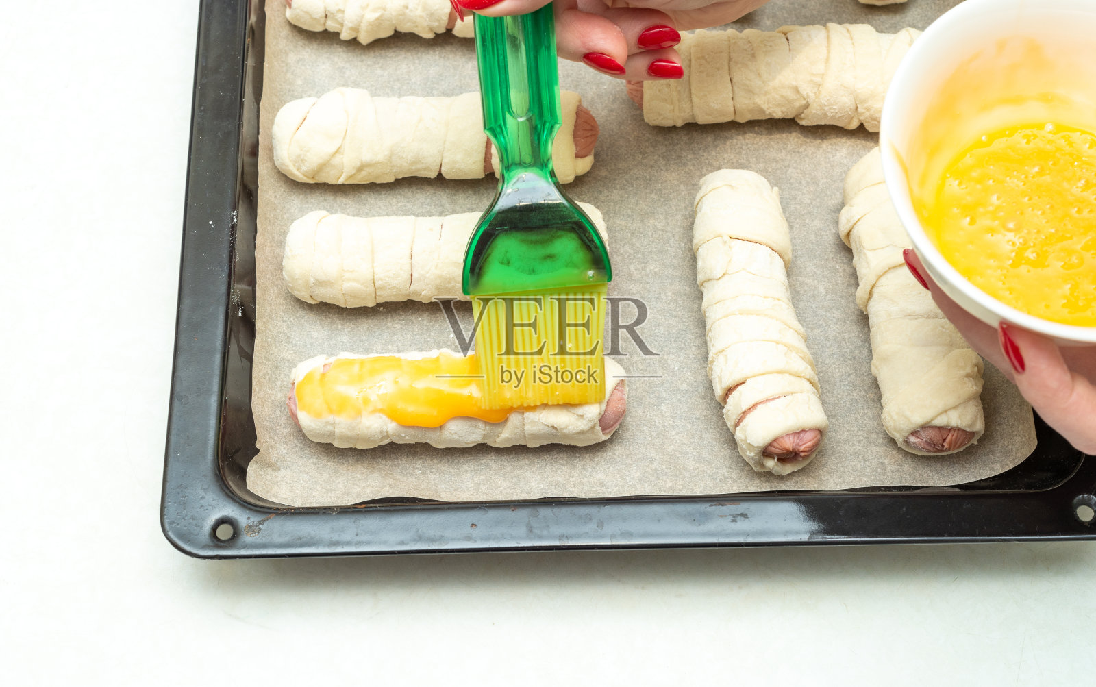 把香肠刷在烤盘上，用生面团条包起来，再涂上蛋黄。照片摄影图片