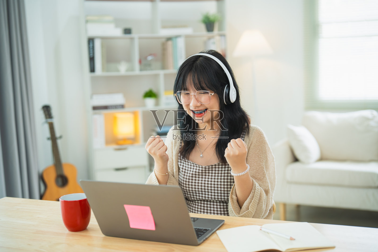 一位戴着眼镜和白色耳机的商业自由企业家愉快地举起手，在笔记本电脑和家庭办公室的桌子上打字。业务技术。照片摄影图片