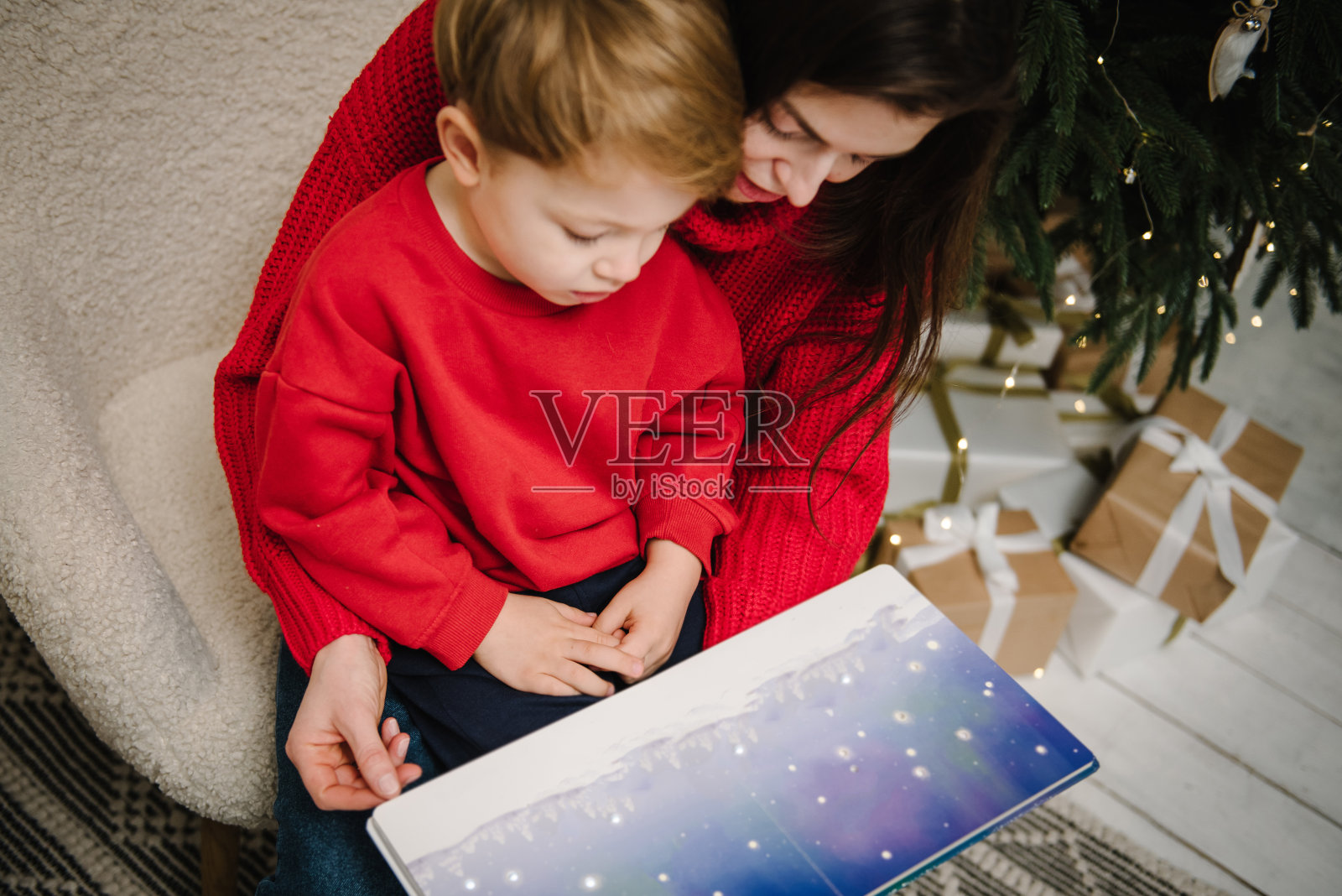 母亲为儿子读书，母子在家中圣诞树旁拥抱照片摄影图片