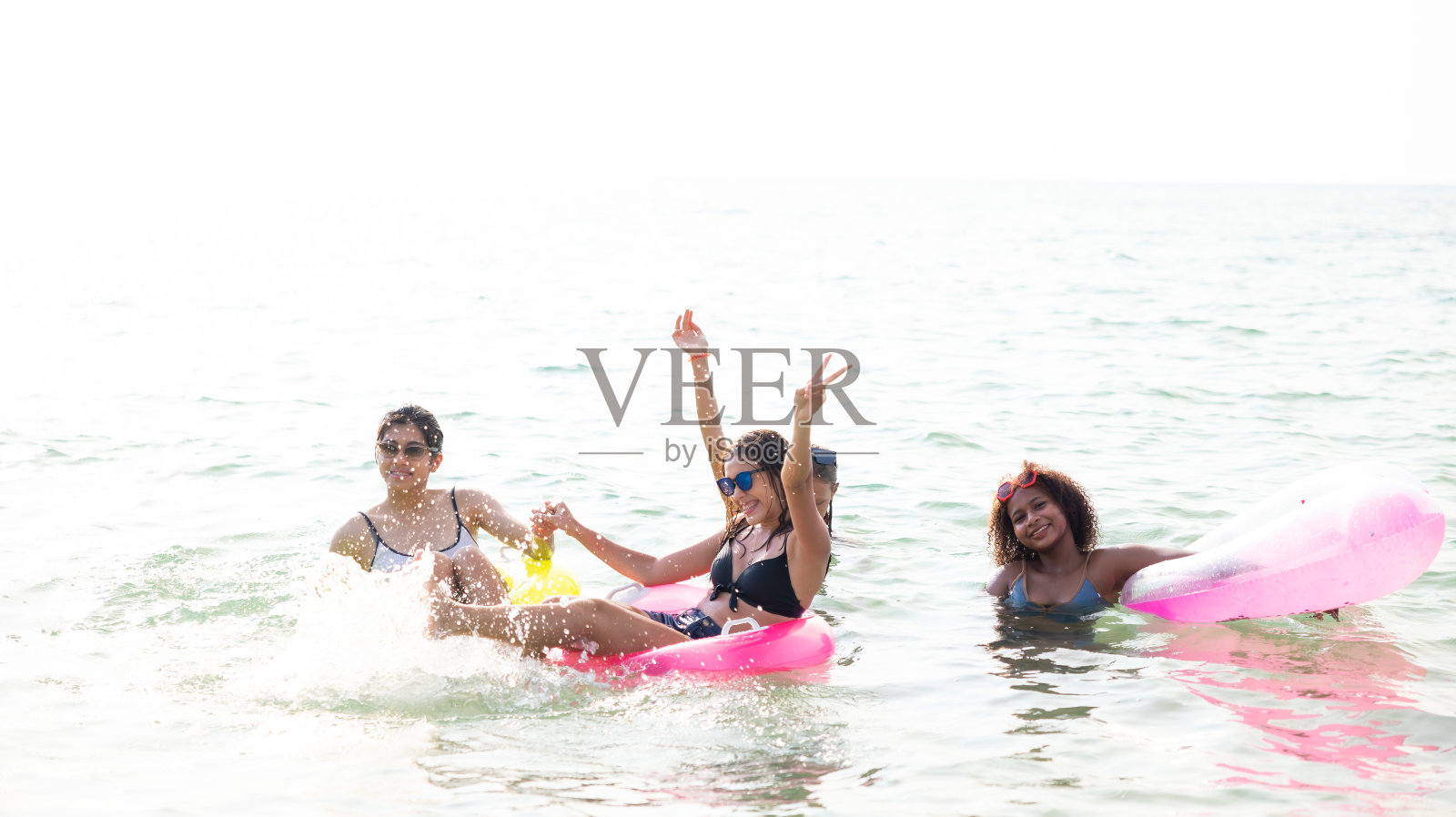 自由浮动。一群不同的少女在海滩上。四个十几岁的女孩在热带海滩上玩充气环。暑假旅行。照片摄影图片