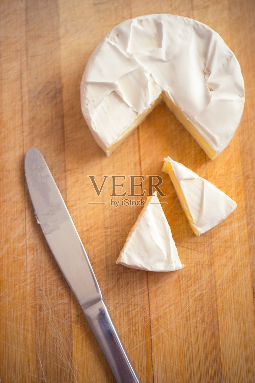 卡曼贝尔奶酪，用三角形切片和一把刀放在木板上。照片摄影图片