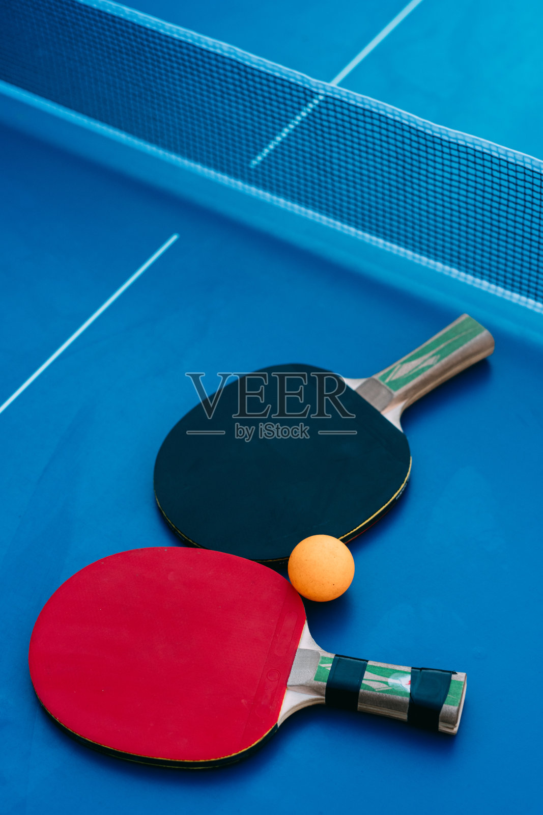 在一张蓝色的网球桌上，有一个黄色球的乒乓球拍。照片摄影图片