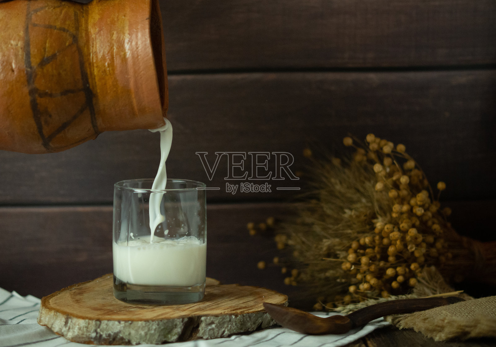 牛奶从一个陶罐倒进一个玻璃杯，背景是质朴的照片摄影图片