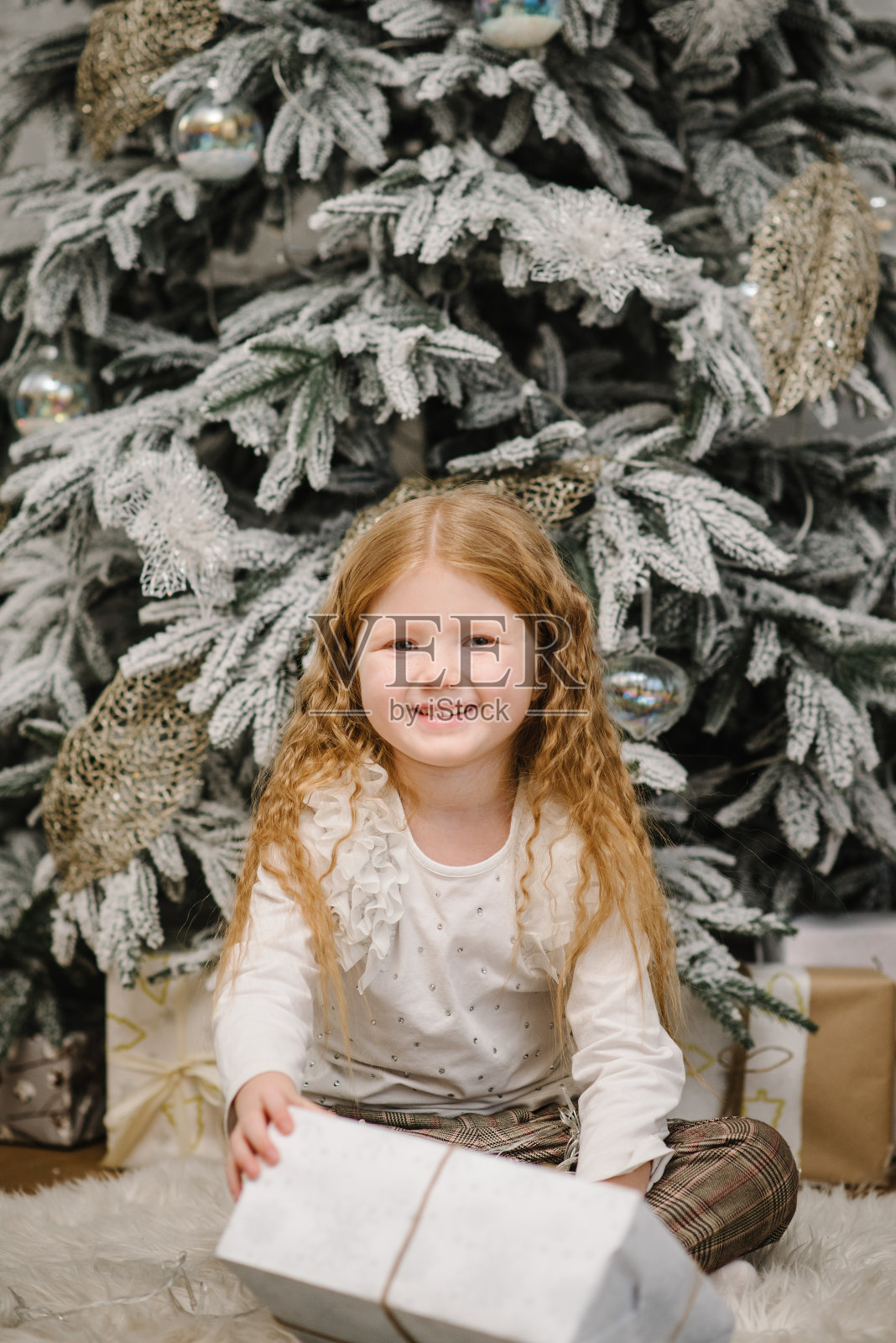 孩子看着并打开魔法盒子，孩子坐在家里的圣诞树旁。快乐微笑的女孩，拿着大大的圣诞礼物。新年的圣诞礼物。室内装饰有花环、彩灯。照片摄影图片