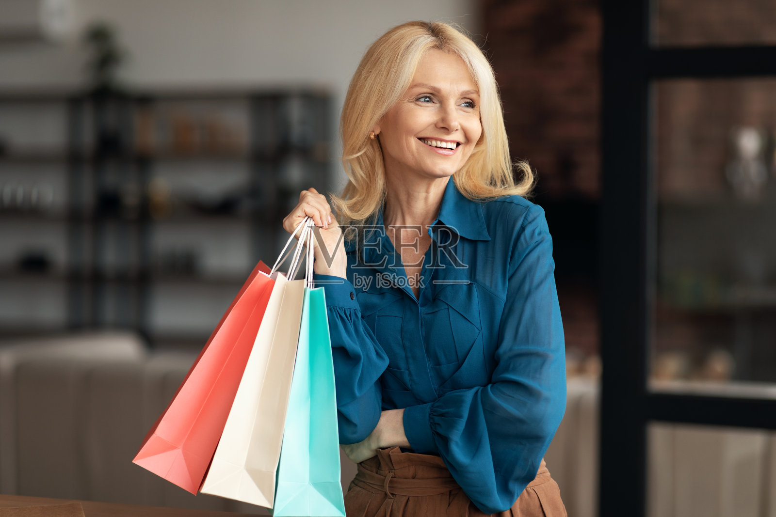 快乐迷人的成熟女人，穿着休闲装b购物狂，拎着五颜六色的购物袋，站在家里，拷贝空间照片摄影图片