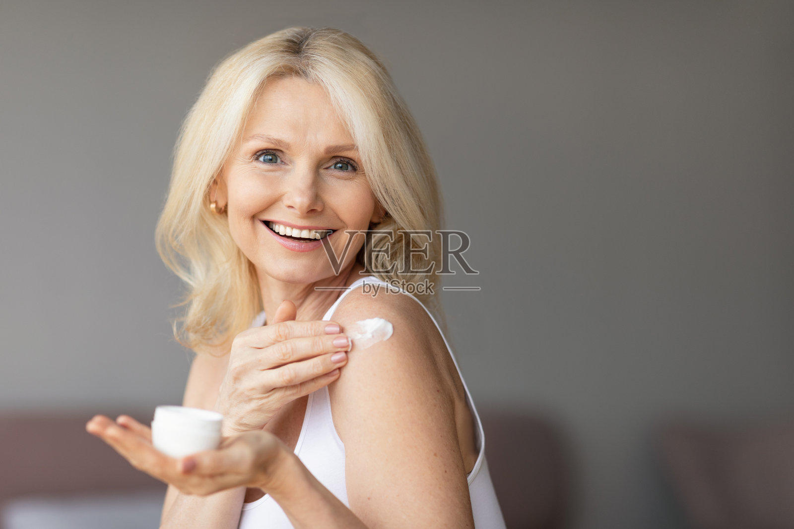 漂亮的成熟女士在沐浴后使用身体乳液或在肩膀上涂抹保湿或滋养霜照片摄影图片