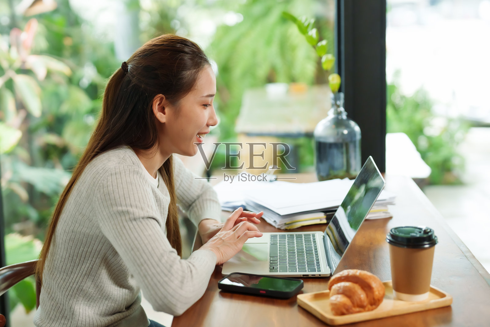 咖啡店老板漂亮的年轻亚洲女人坐在办公桌前的笔记本电脑前。在一个小咖啡店里和朋友在线视频通话照片摄影图片