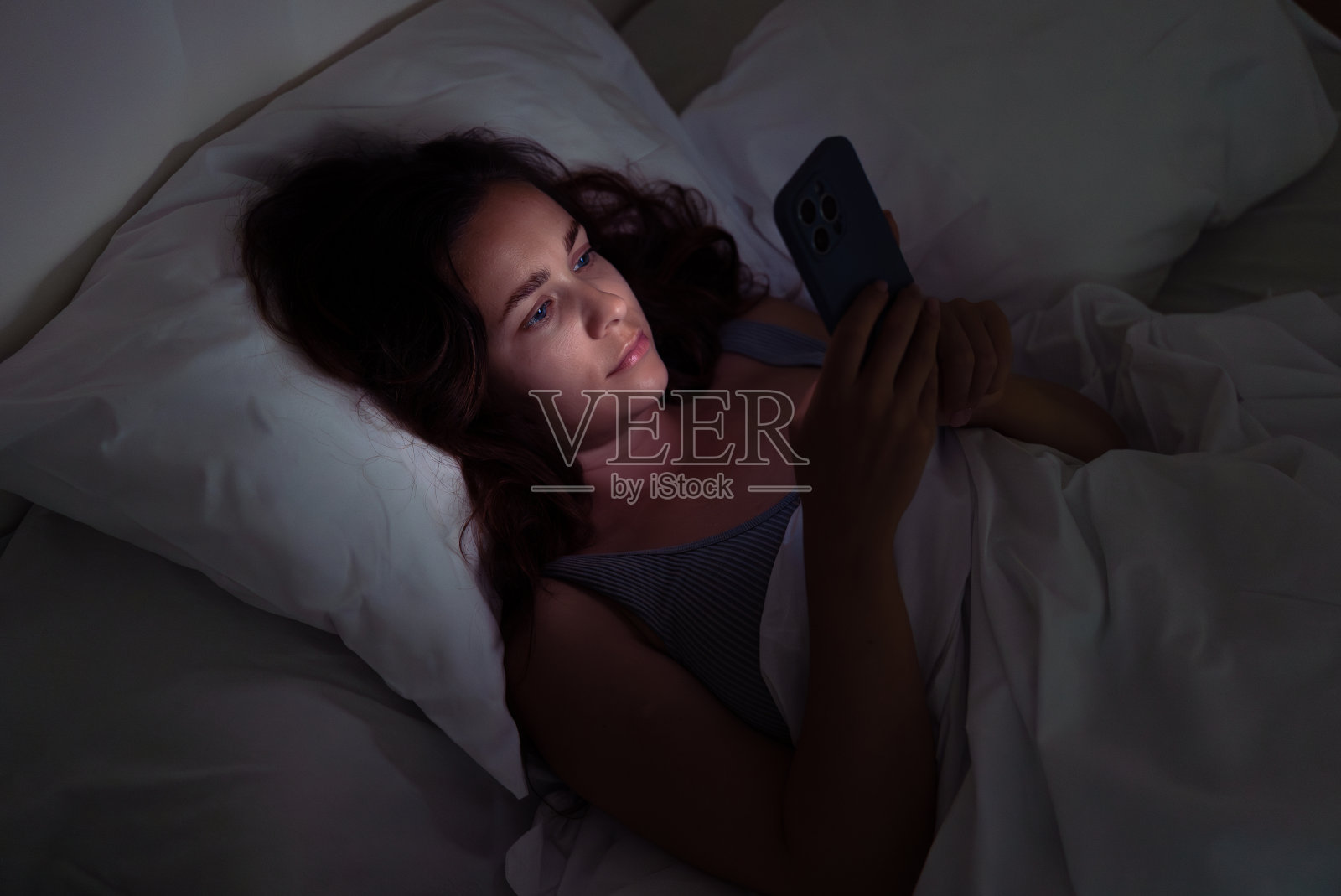 深夜躺在床上的女人，沉迷于手机屏幕、失眠和对智能手机的依赖。照片摄影图片