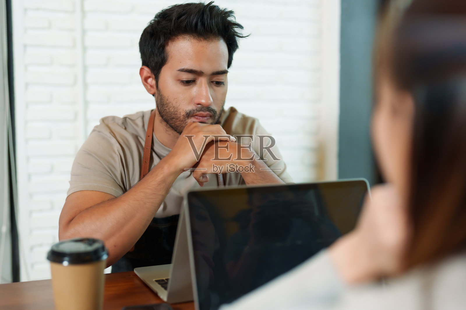 留着小胡子的印度人咖啡店老板坐在那对工作的夫妇对面的笔记本电脑前，一边查看着店里的收入和支出，一边沉思着，他的表情很紧张。照片摄影图片