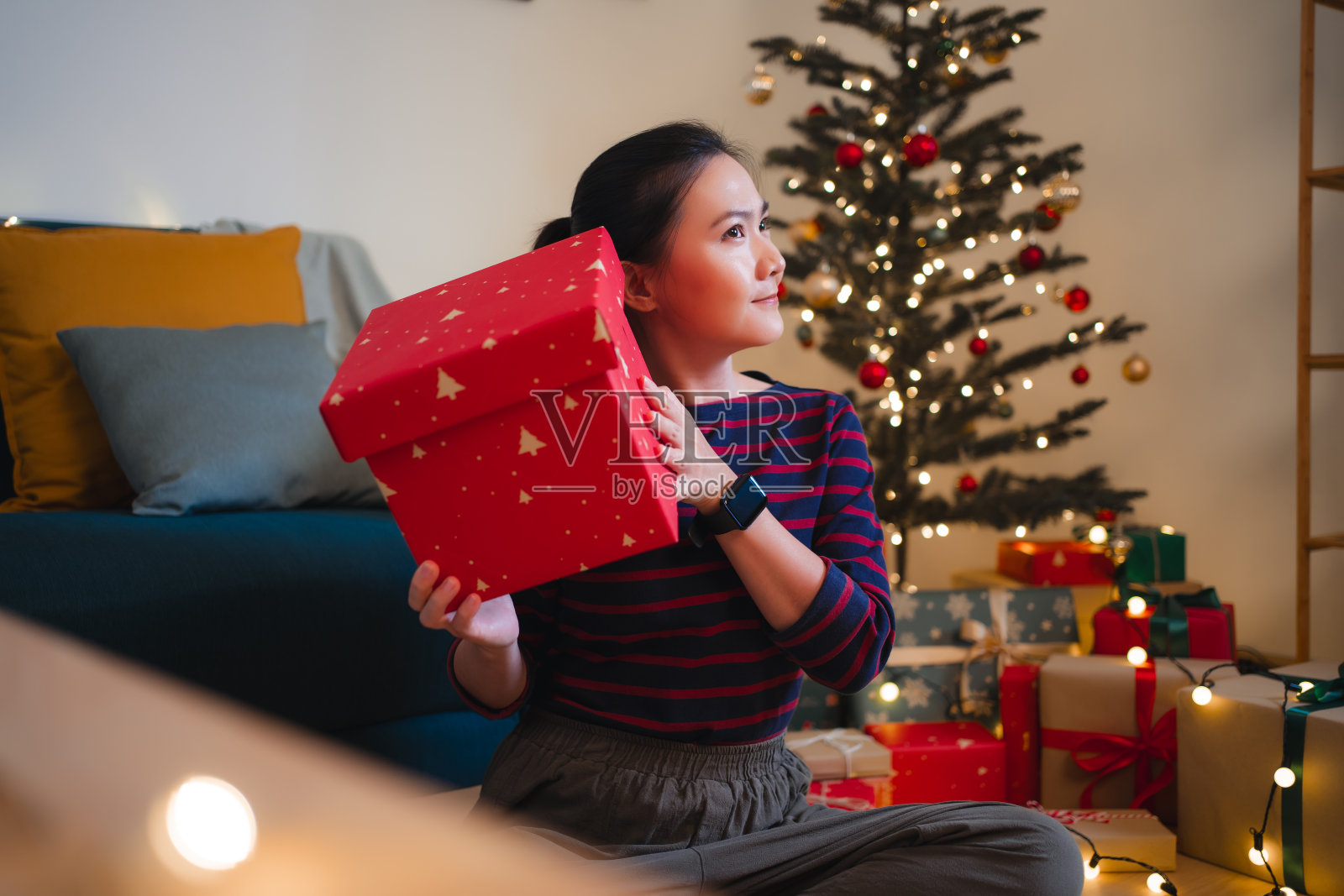 亚洲女子兴奋地摇着圣诞礼盒好奇地说。照片摄影图片