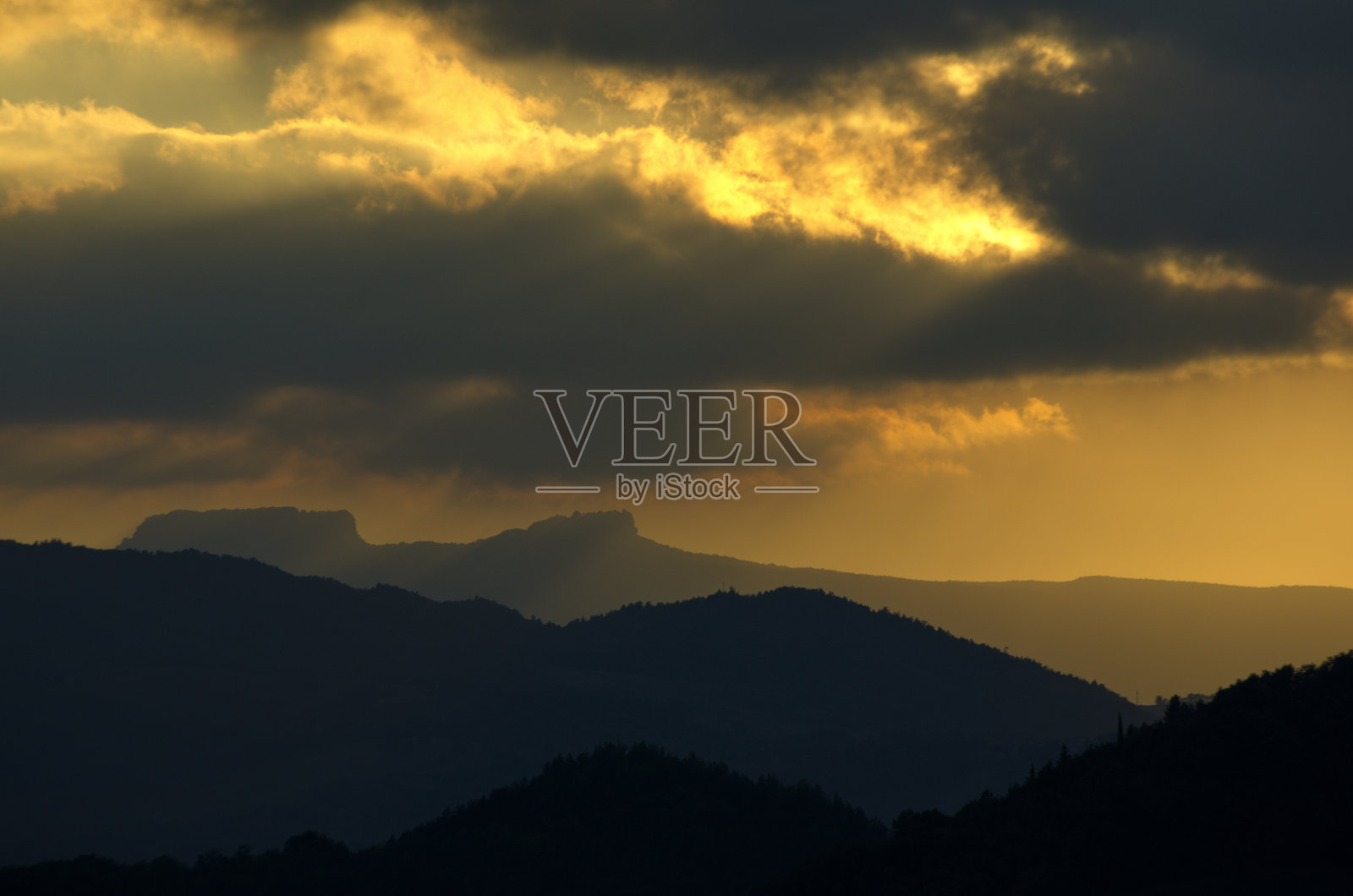 落日余晖映衬着多云天空的群山轮廓照片摄影图片