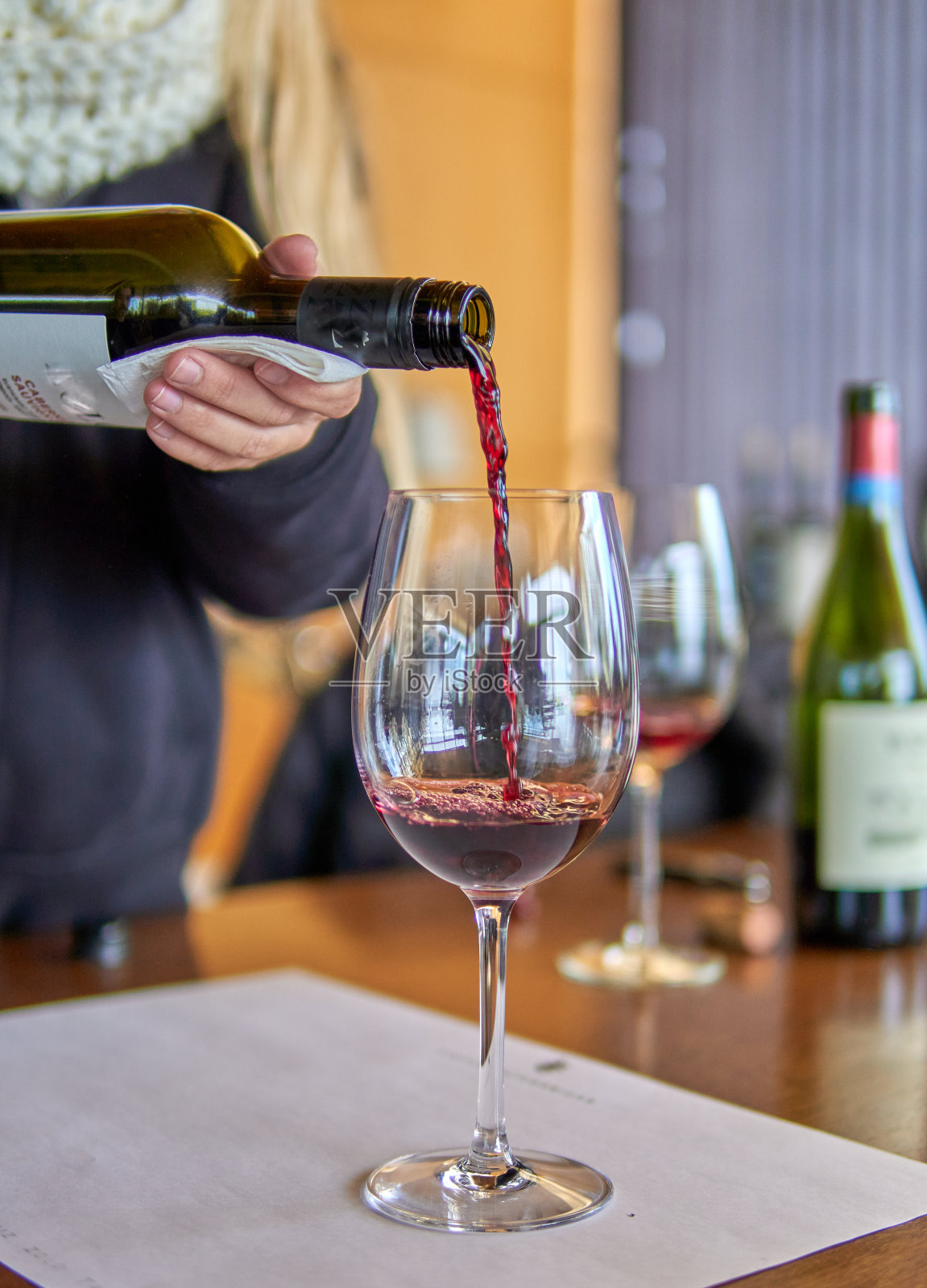 在阿根廷门多萨品尝葡萄酒。女人手里捧着一瓶红酒倒进玻璃杯里。模糊的背景。有选择性的重点照片摄影图片